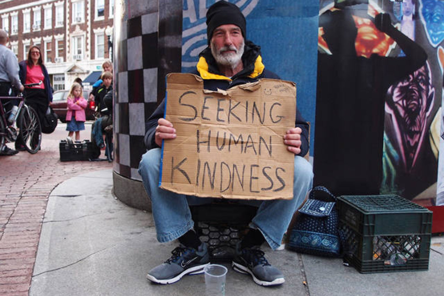 Homeless man holding sign that says "seeking human kindness"