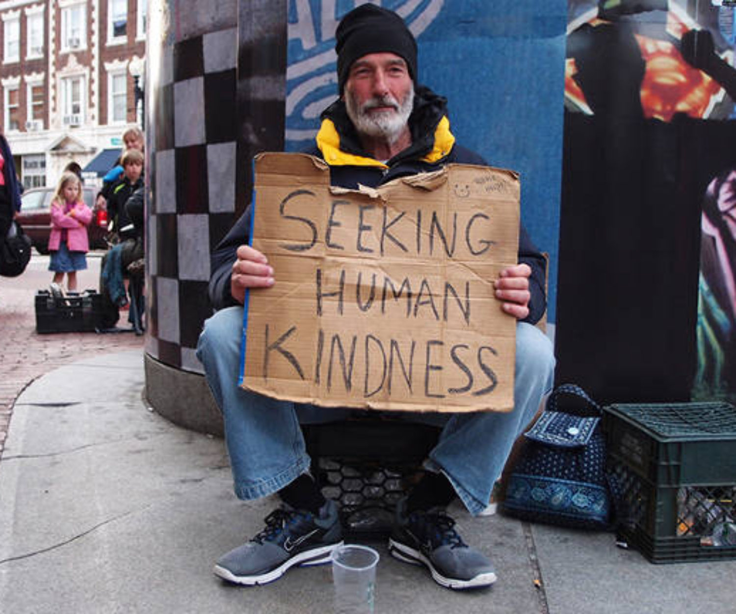 Homeless man holding sign that says "seeking human kindness"